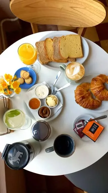 Mesa de desayuno con café con leche, jugo de naranja, tostadas con untables y medialunas