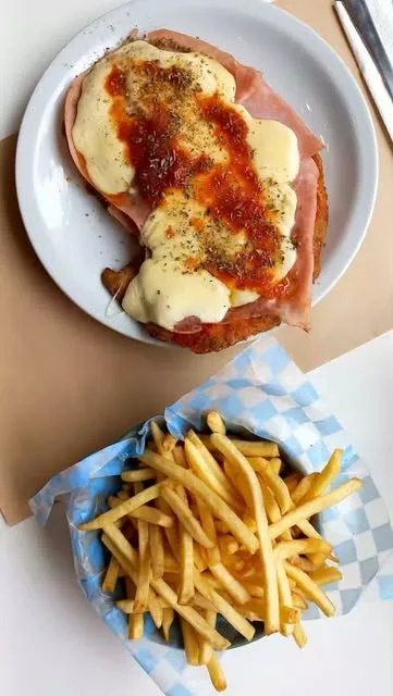 Milanesa a la napolitana con jamón, queso y salsa, junto a una canasta de papas fritas