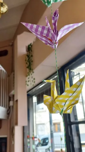 Grullas de origami de papel a cuadros colgando junto a la ventana del local